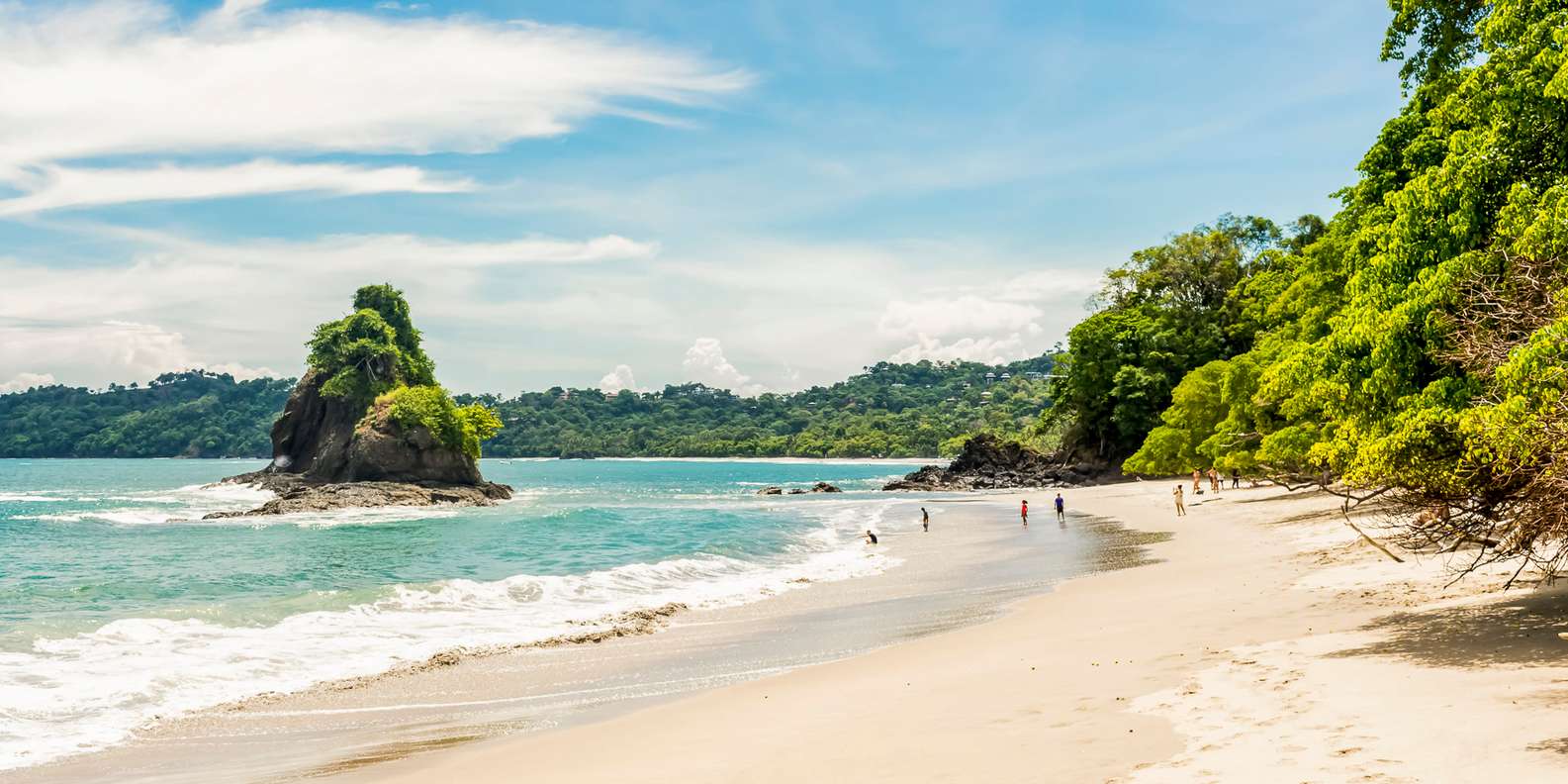 White-sand beach at Manuel Antonio, with rainforest reaching the shore and a forested rock islet offshore